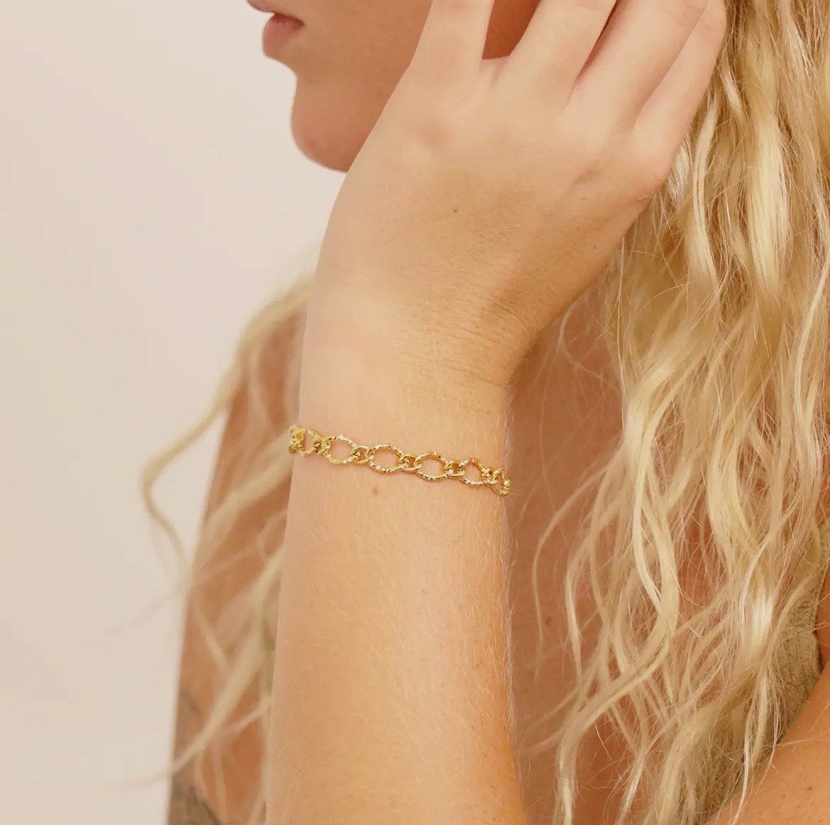 Gold chain bracelet on a wrist with a neutral background