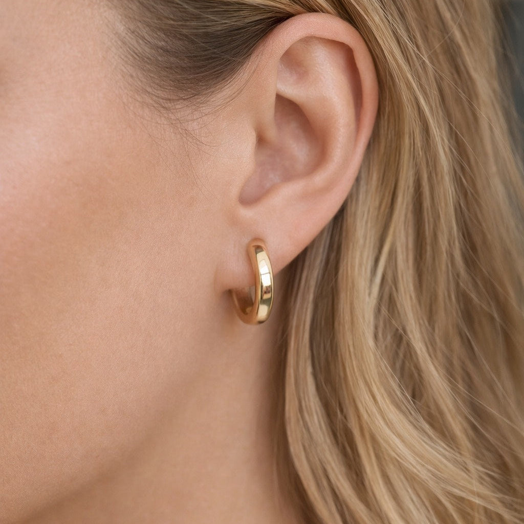 Close-up of a person wearing a gold hoop earring with blurred background