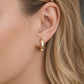 Close-up of a person wearing a gold hoop earring with blurred background
