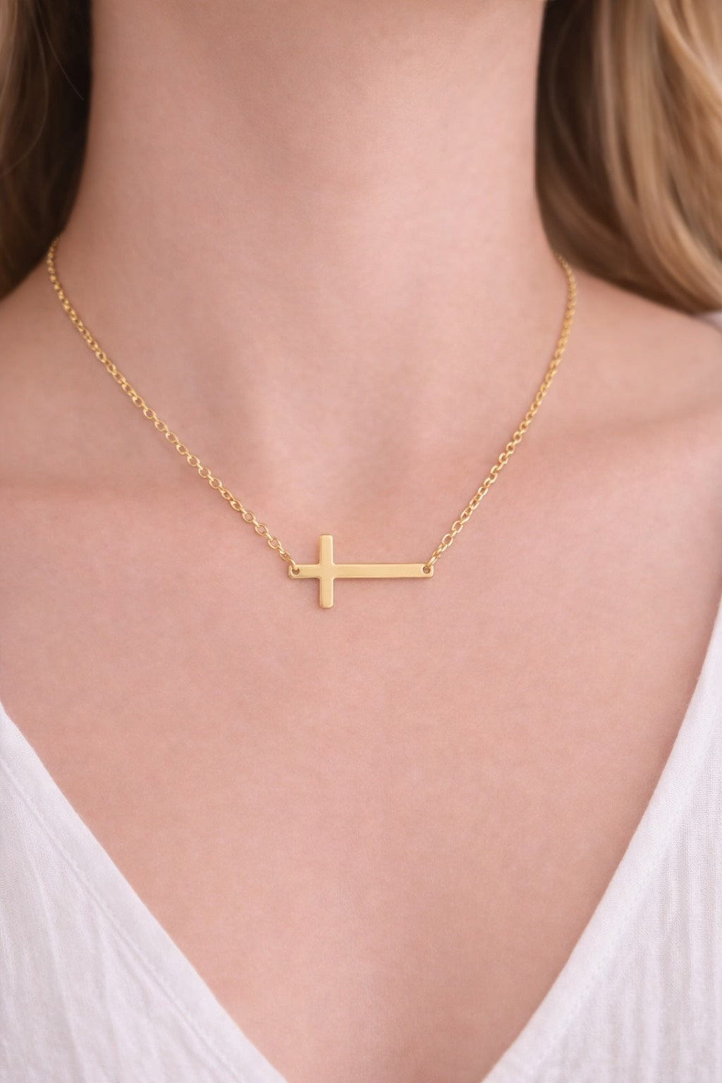 Gold cross necklace on a person wearing a white top