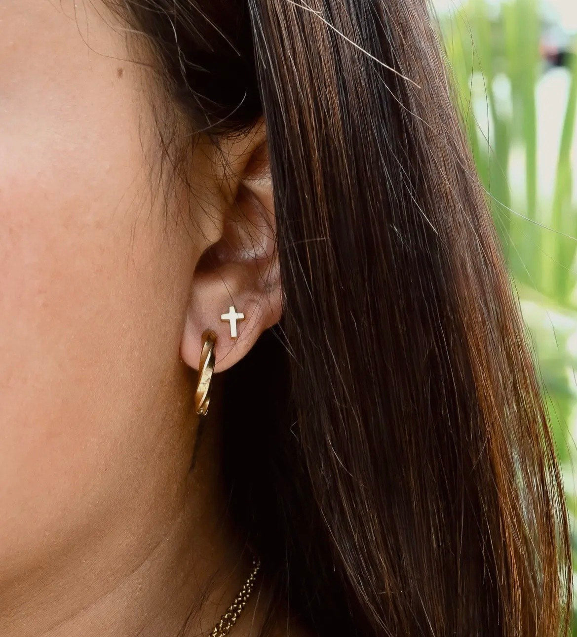 Close-up of an ear wearing a gold hoop earring with a small cross detail.