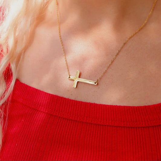 Gold necklace with a cross pendant worn by a person in a red top.